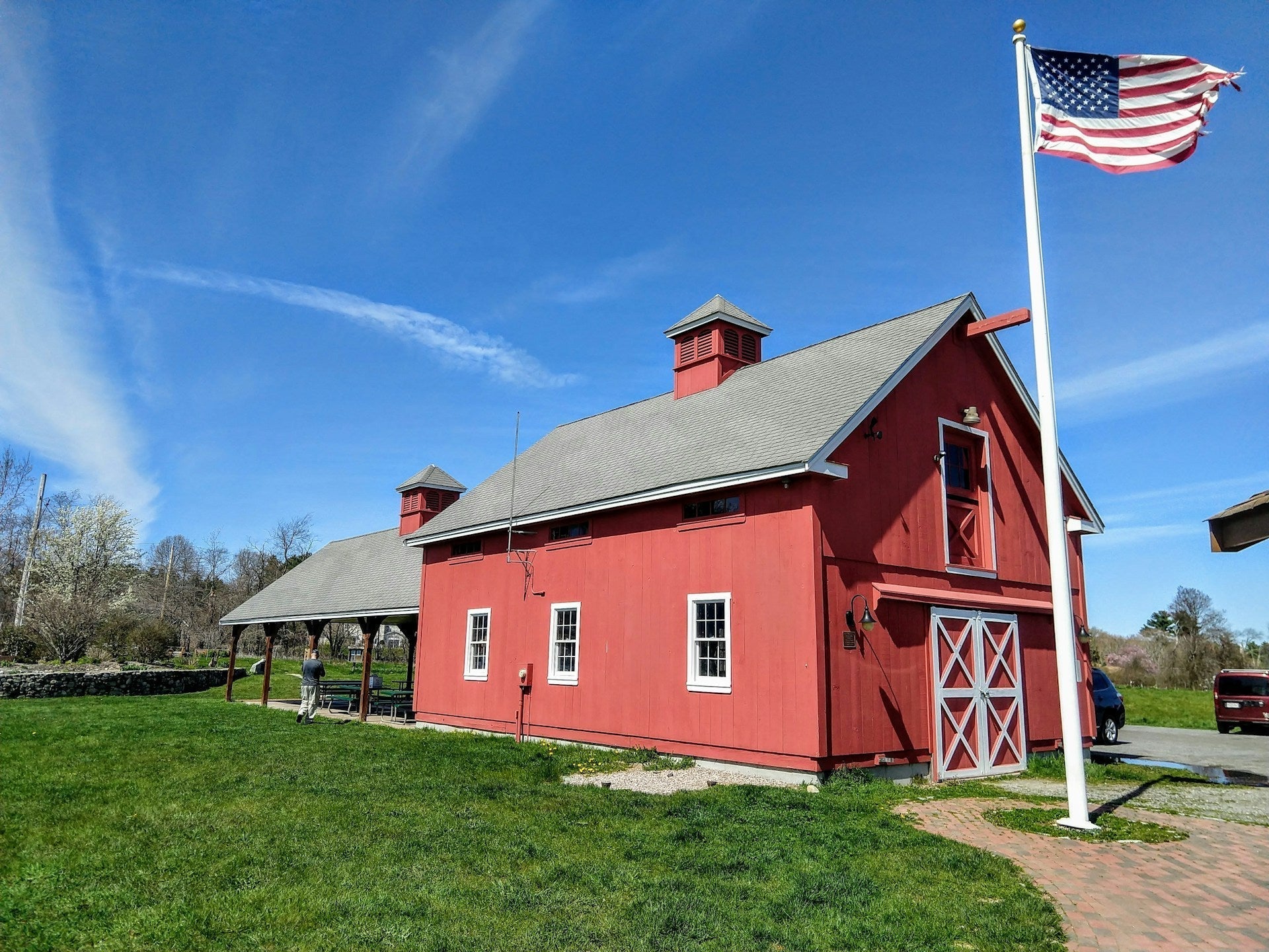 large American flag on tall flagpole beside red barn on rural property