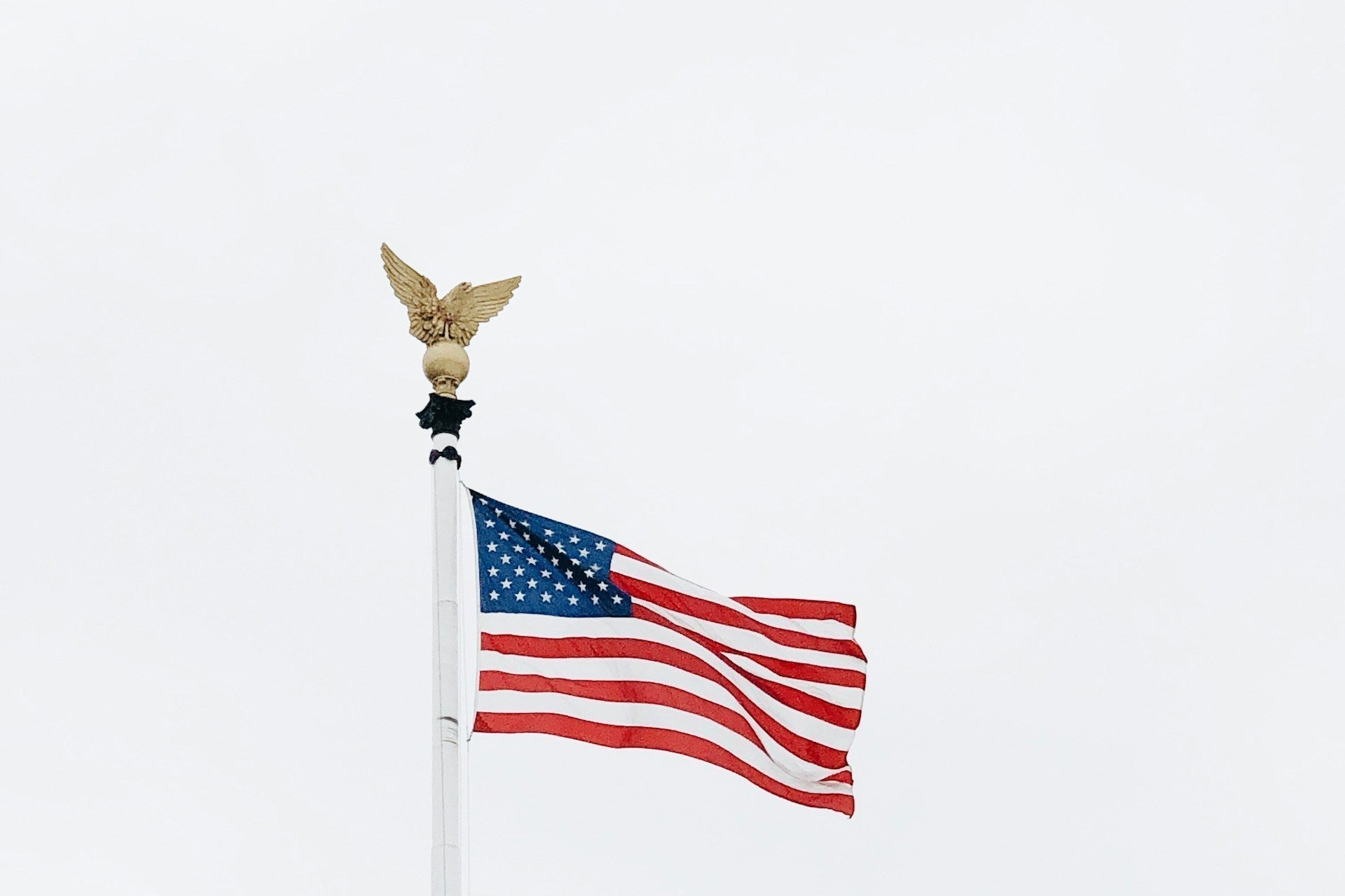 American flag on a white pole with gold eagle finial against cloudy sky
