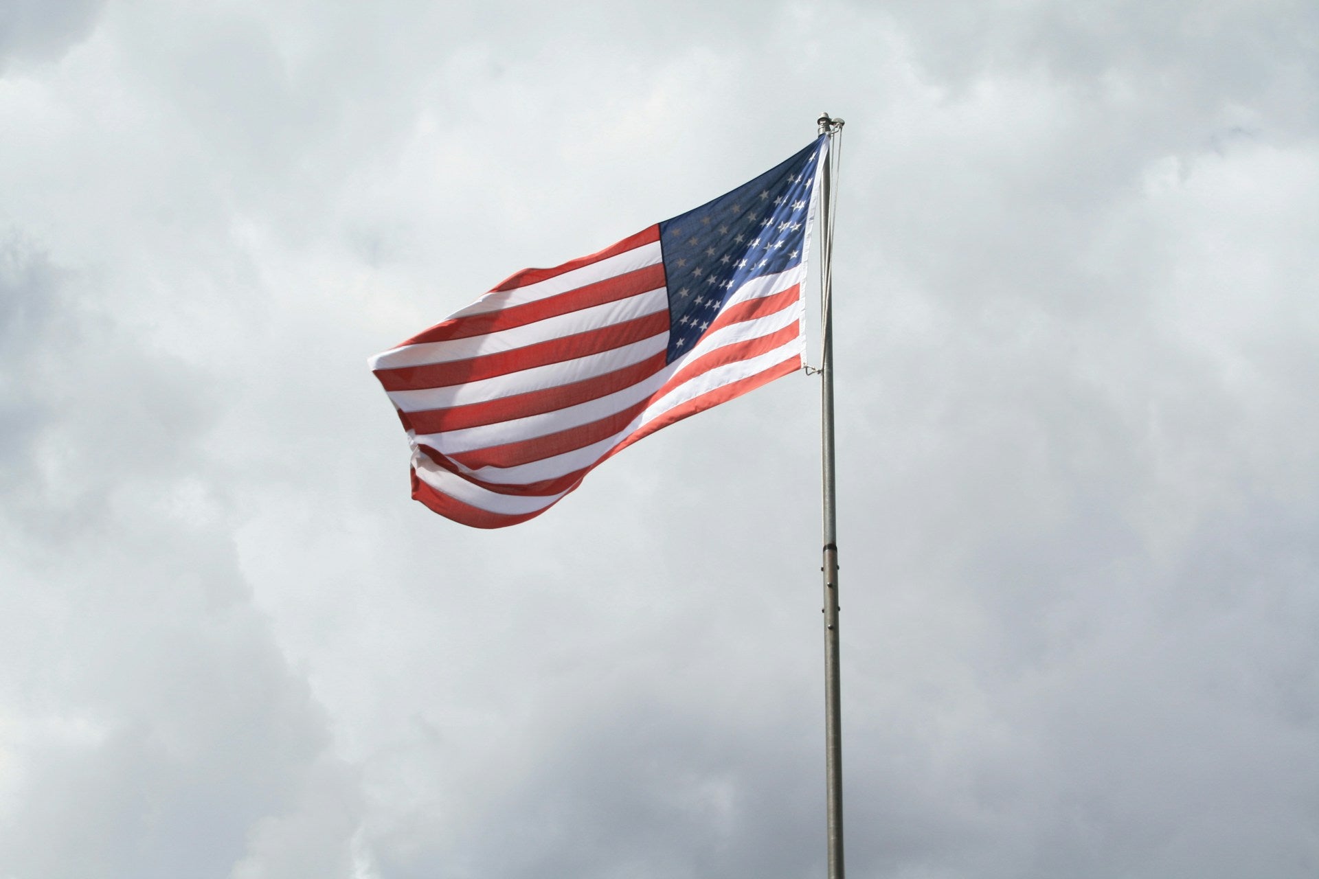 Tall American flagpole flying USA flag in a stormy cloudy sky