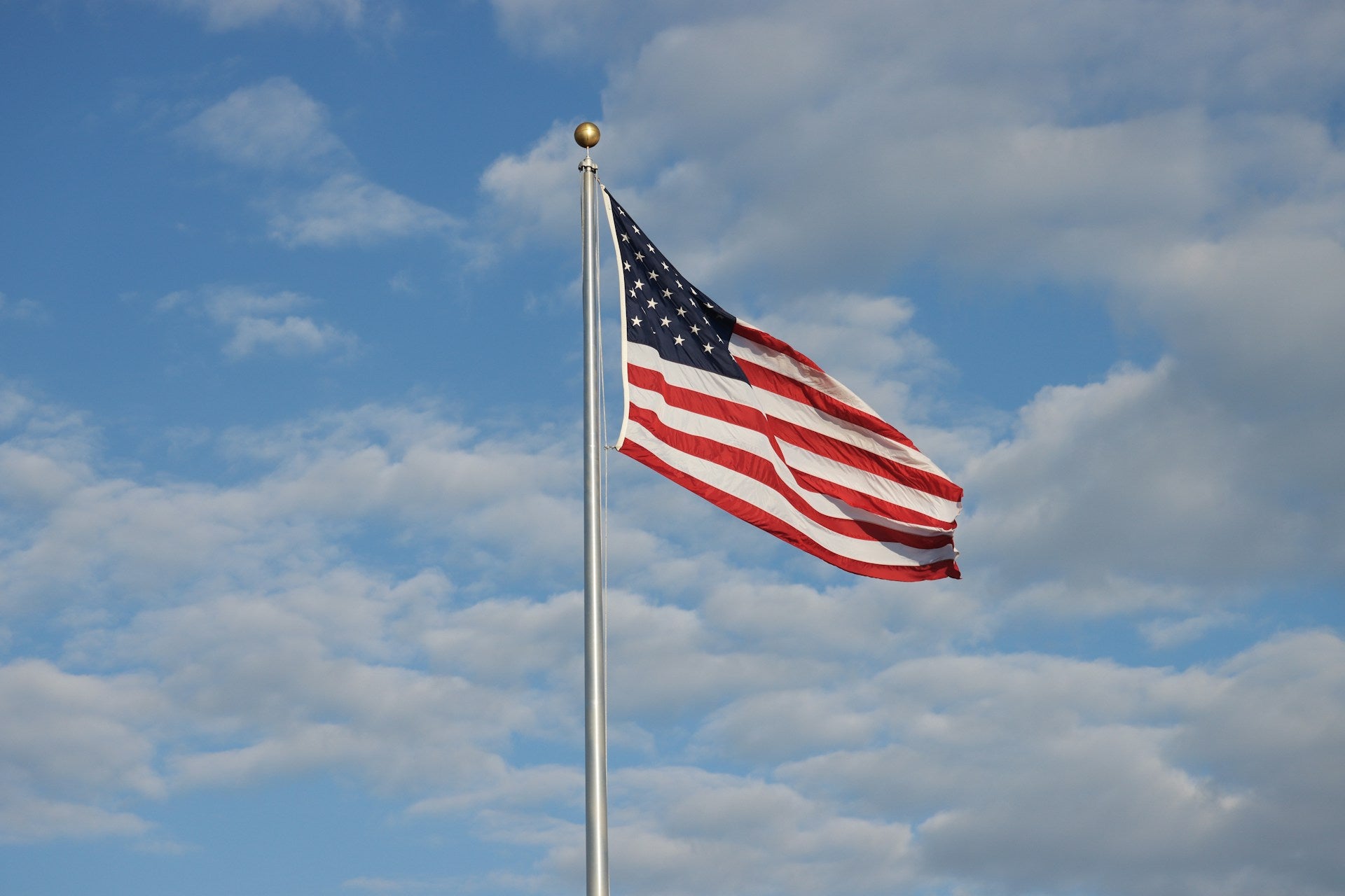 American flag flying on tall flagpole against blue sky with clouds