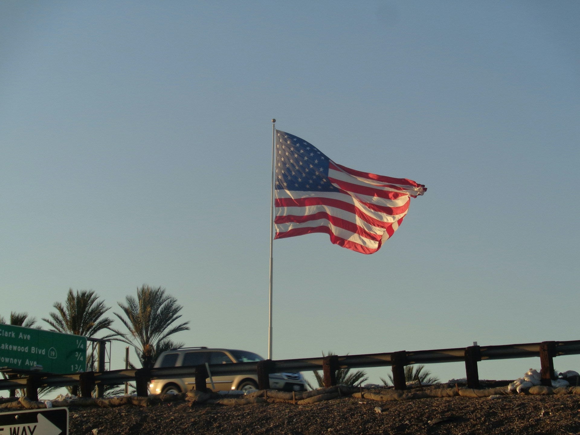 American flag flying on portable flagpole beside RV at forest campsite under clear blue sky