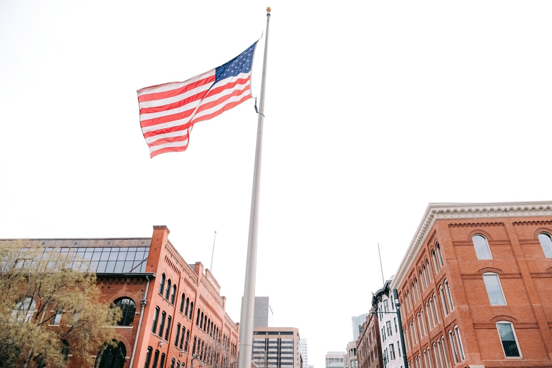 USA flag flying on a tall flagpole above historic city buildings, symbolizing national pride.